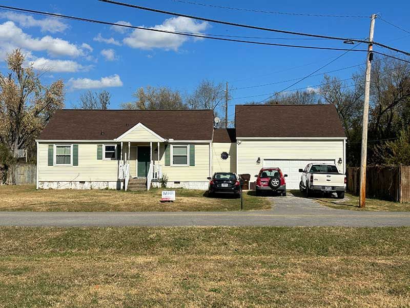 A white house with a brown roof and two cars parked in front of it.