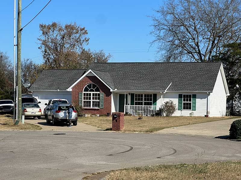 Two cars are parked in front of a white house with a gray roof.
