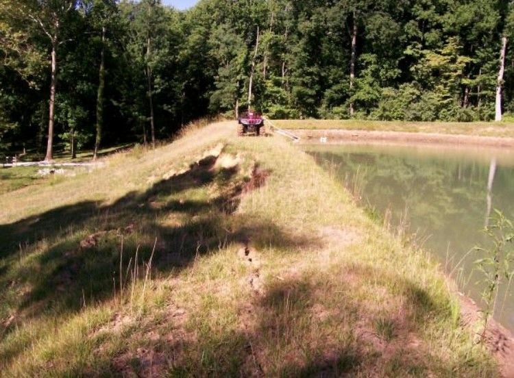 A tractor is parked next to a pond in the woods.