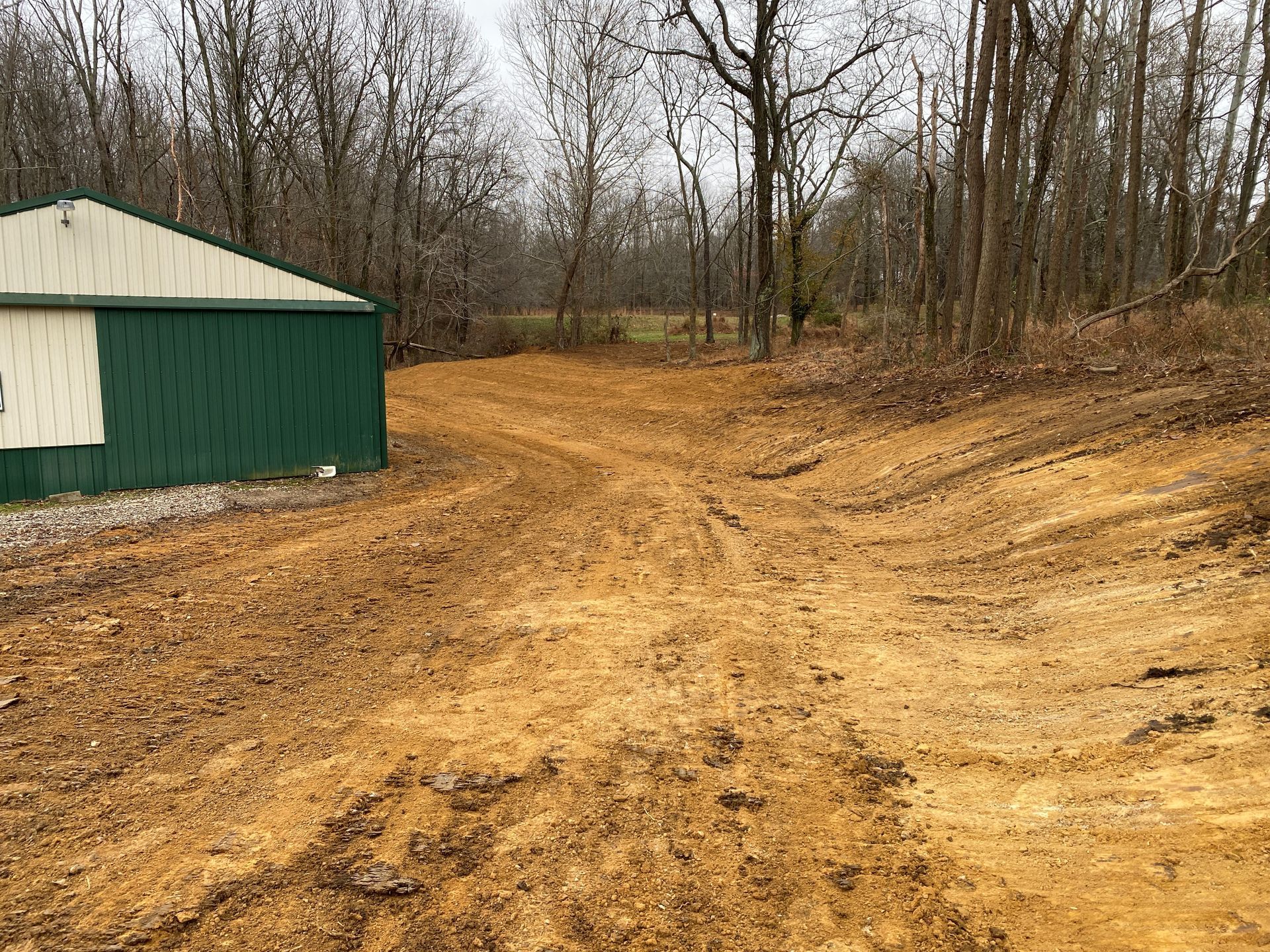 A dirt road leading to a green building in the woods.