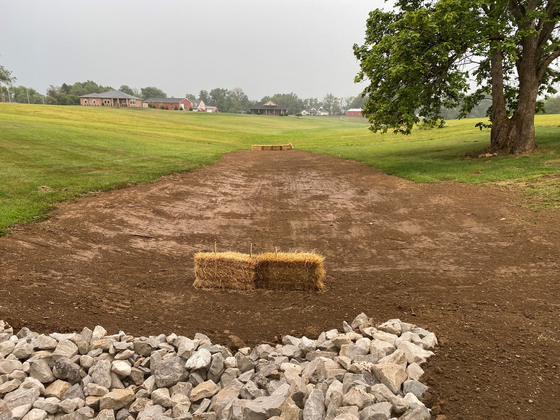 A hay bale is sitting in the middle of a dirt road next to a pile of rocks.