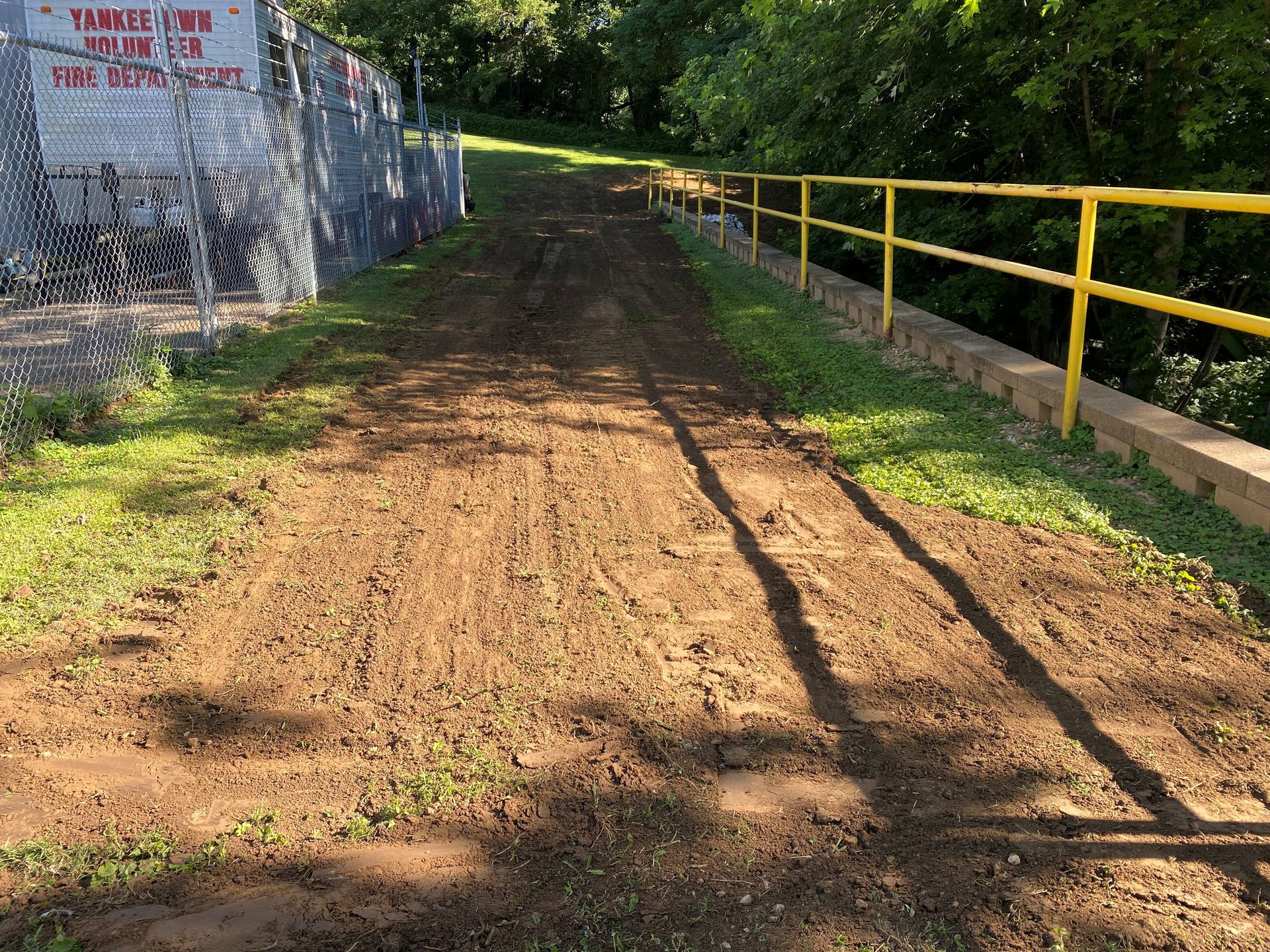 A dirt road with a yellow railing and a fence in the background.
