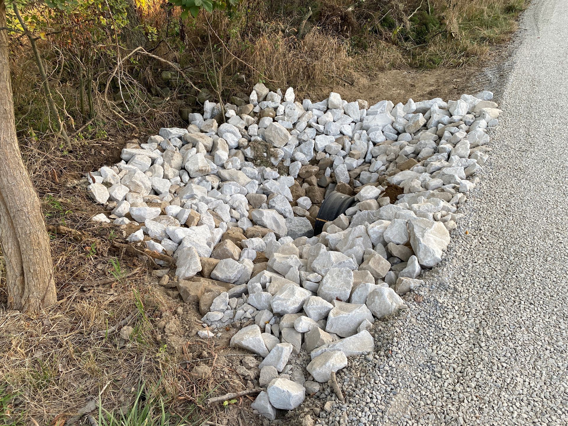 A pile of rocks on the side of a road next to a tree.