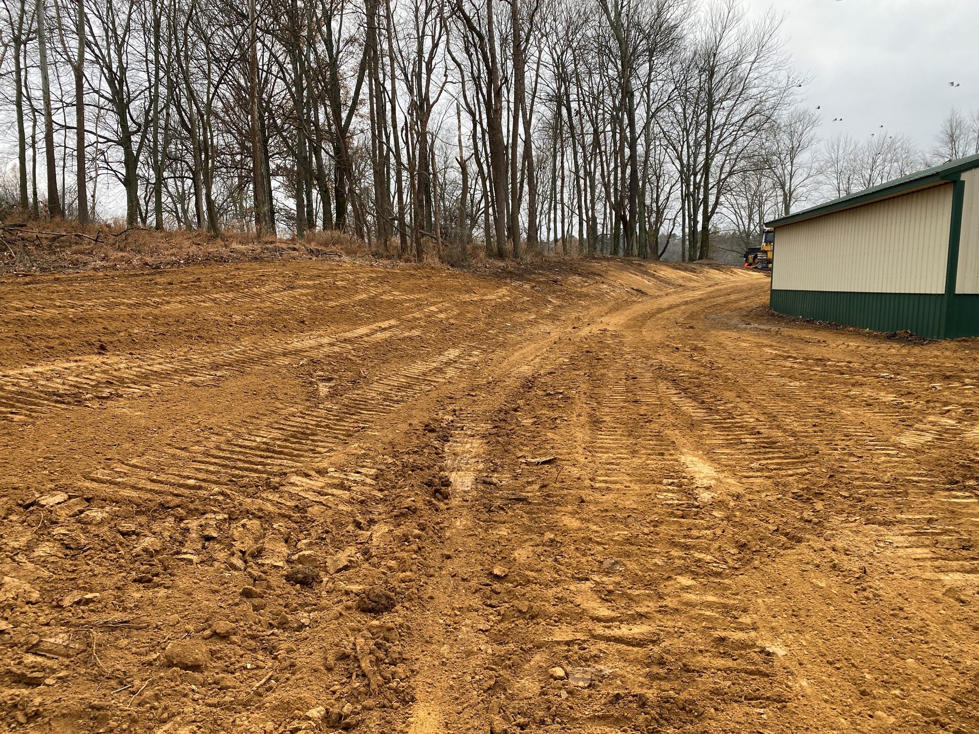 A dirt road leading to a building with trees in the background.