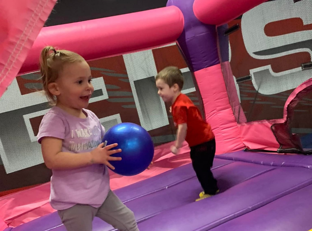 A boy and a girl are playing with a ball in a bouncy house.