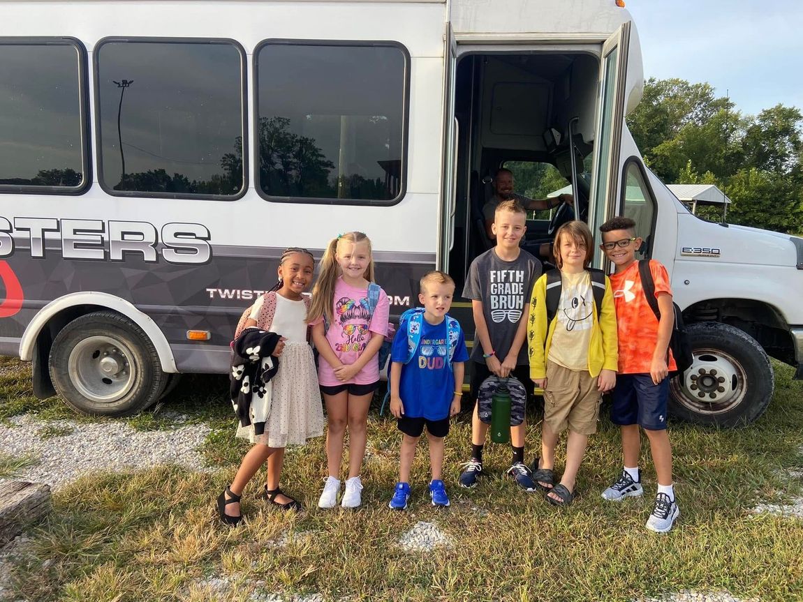 A group of children are standing in front of a bus.