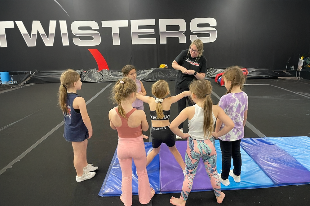 A group of young girls are standing in a circle on a mat in front of a sign that says twisters.