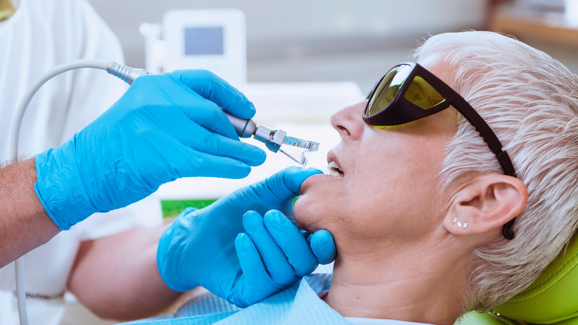 A woman is sitting in a dental chair getting her teeth examined by a dentist.