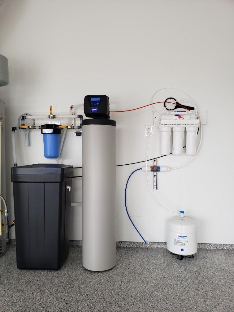 Man in blue uniform and cap installs a white water heater on a concrete wall.