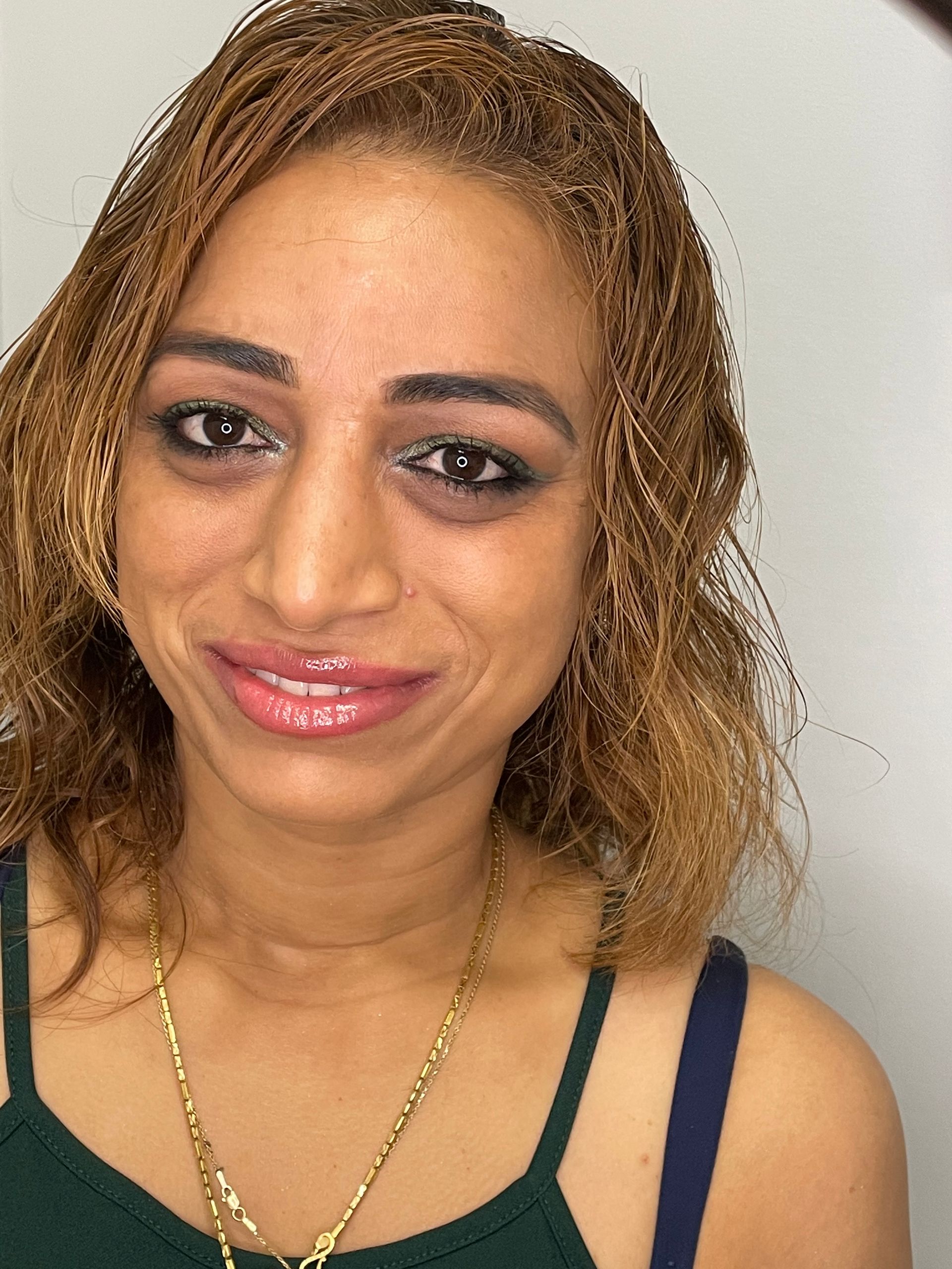 A woman wearing a green tank top and a gold chain smiles for the camera.