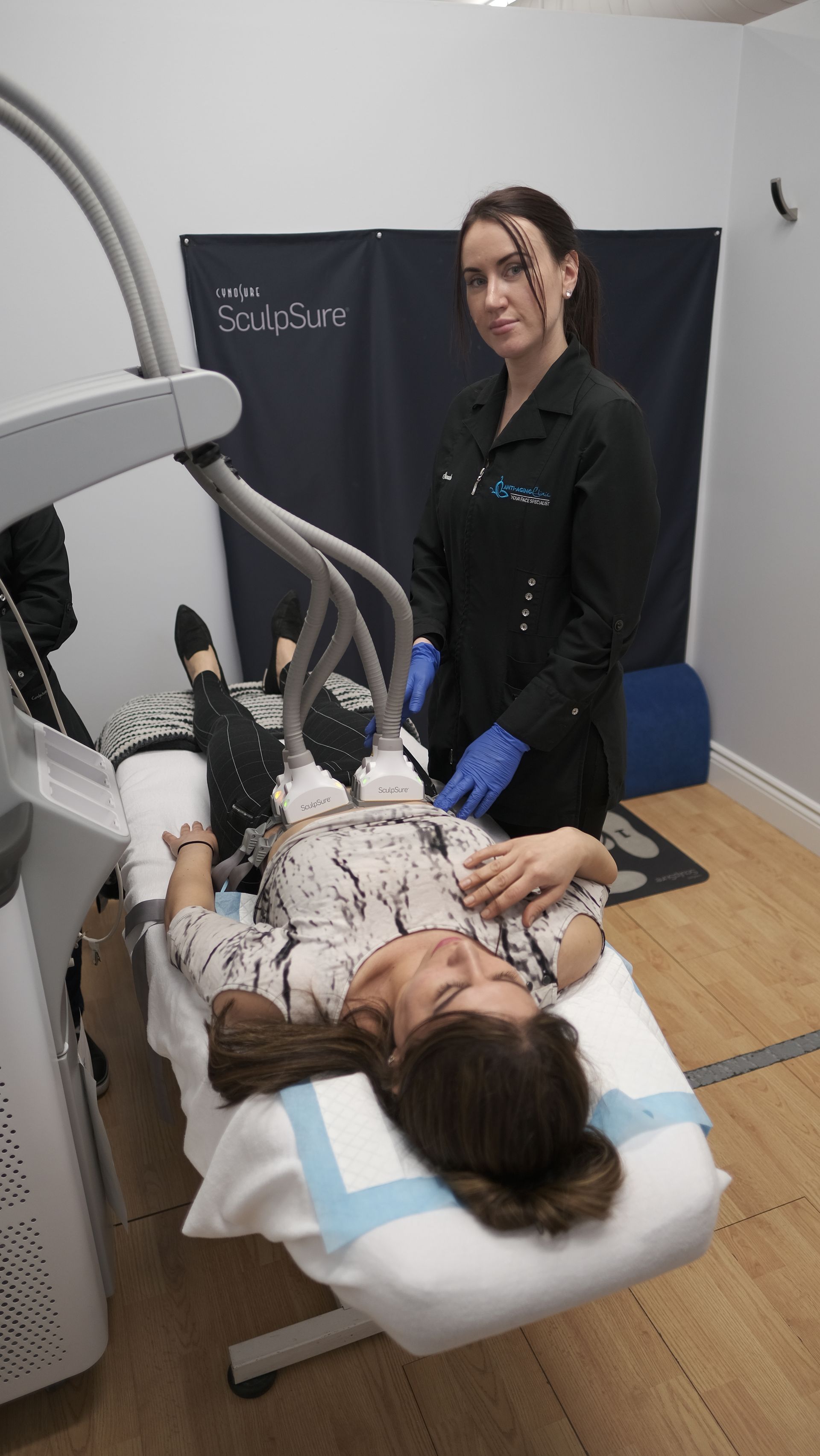 Two women are standing next to a woman laying on a bed.