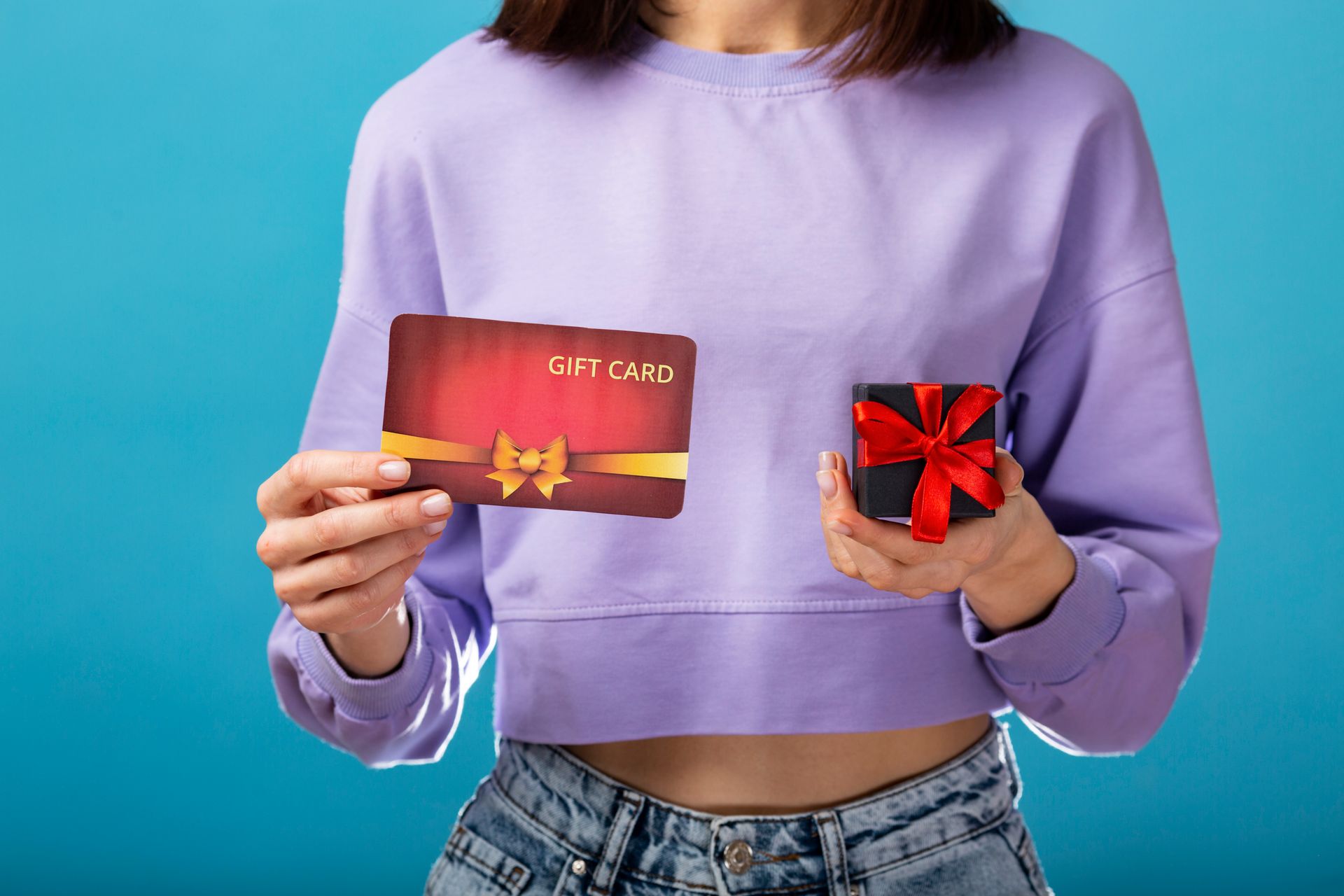 Woman in purple holding gift card and small gift box against a blue backdrop.