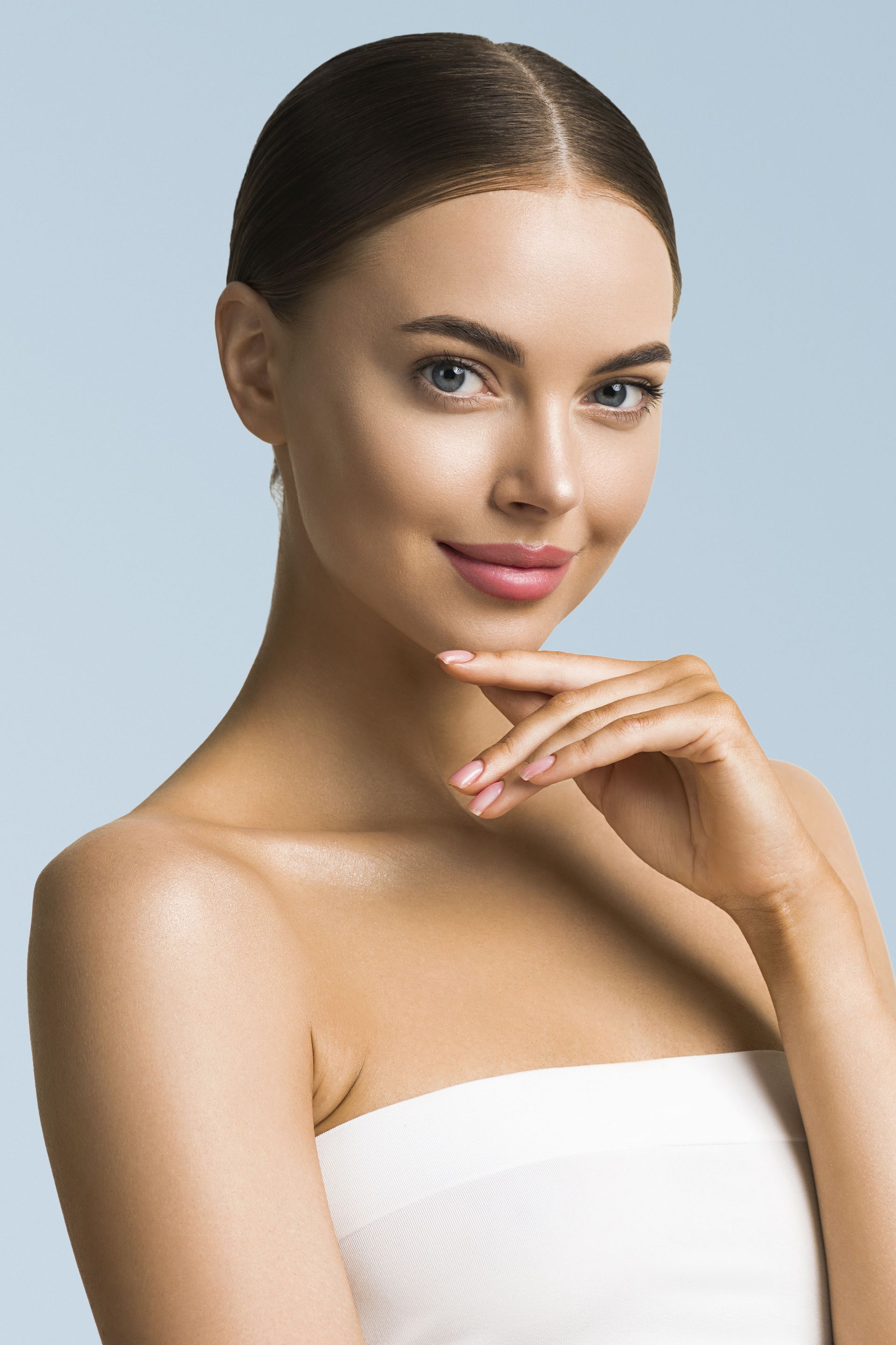 A woman wrapped in a white towel is smiling and touching her face.