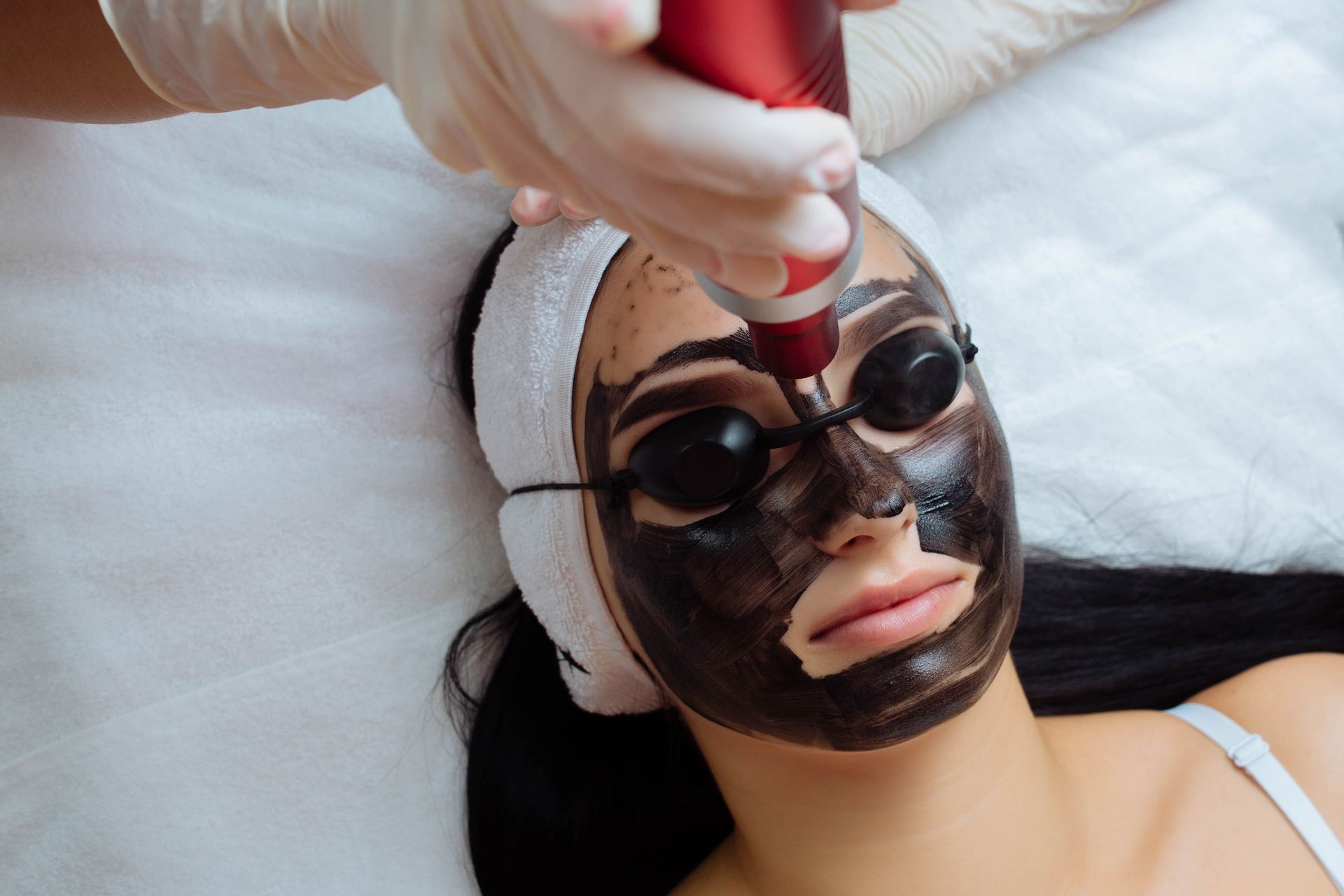 A woman is getting a black mask on her face.