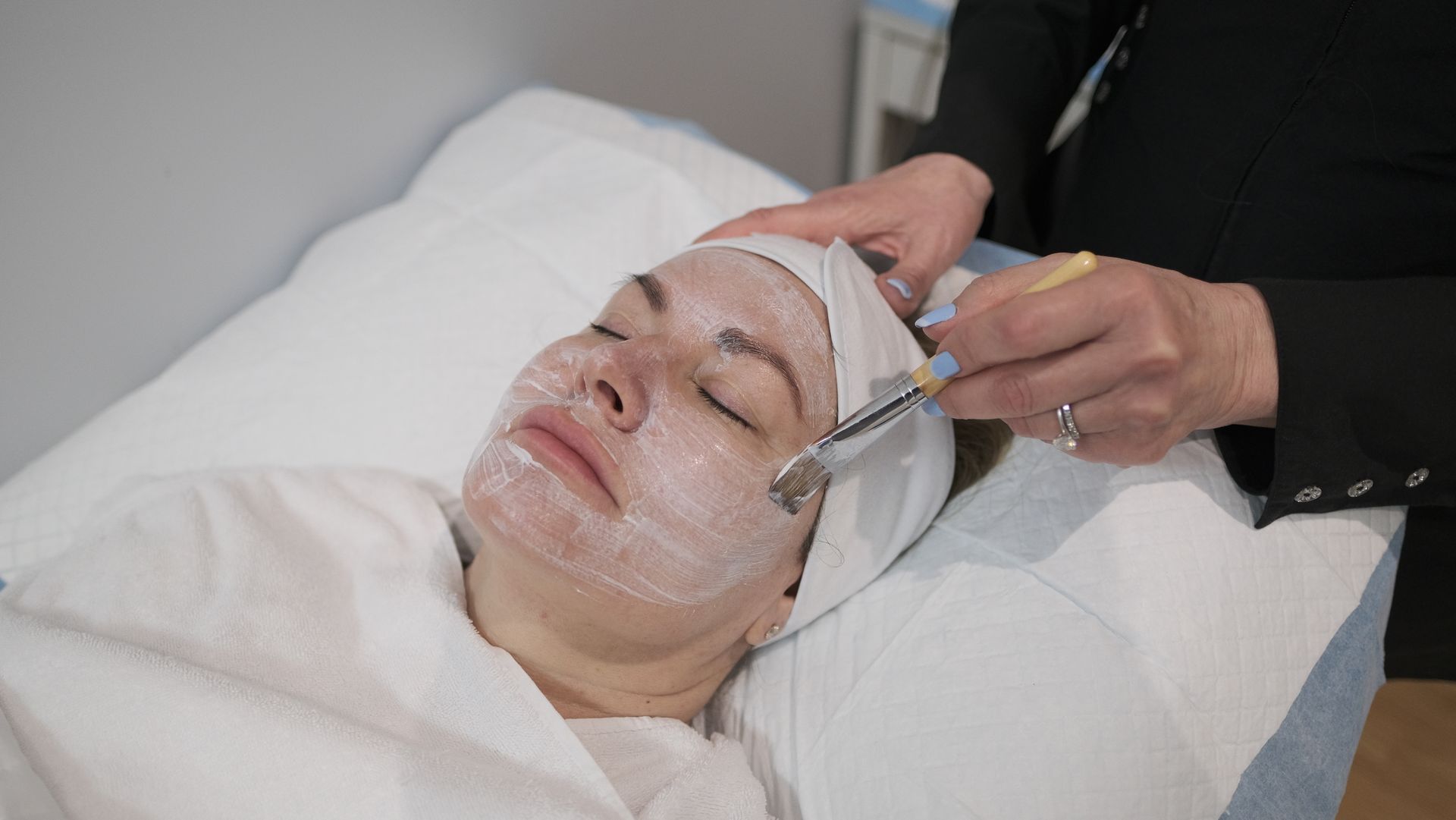 A woman is getting a facial treatment with a brush on her face.