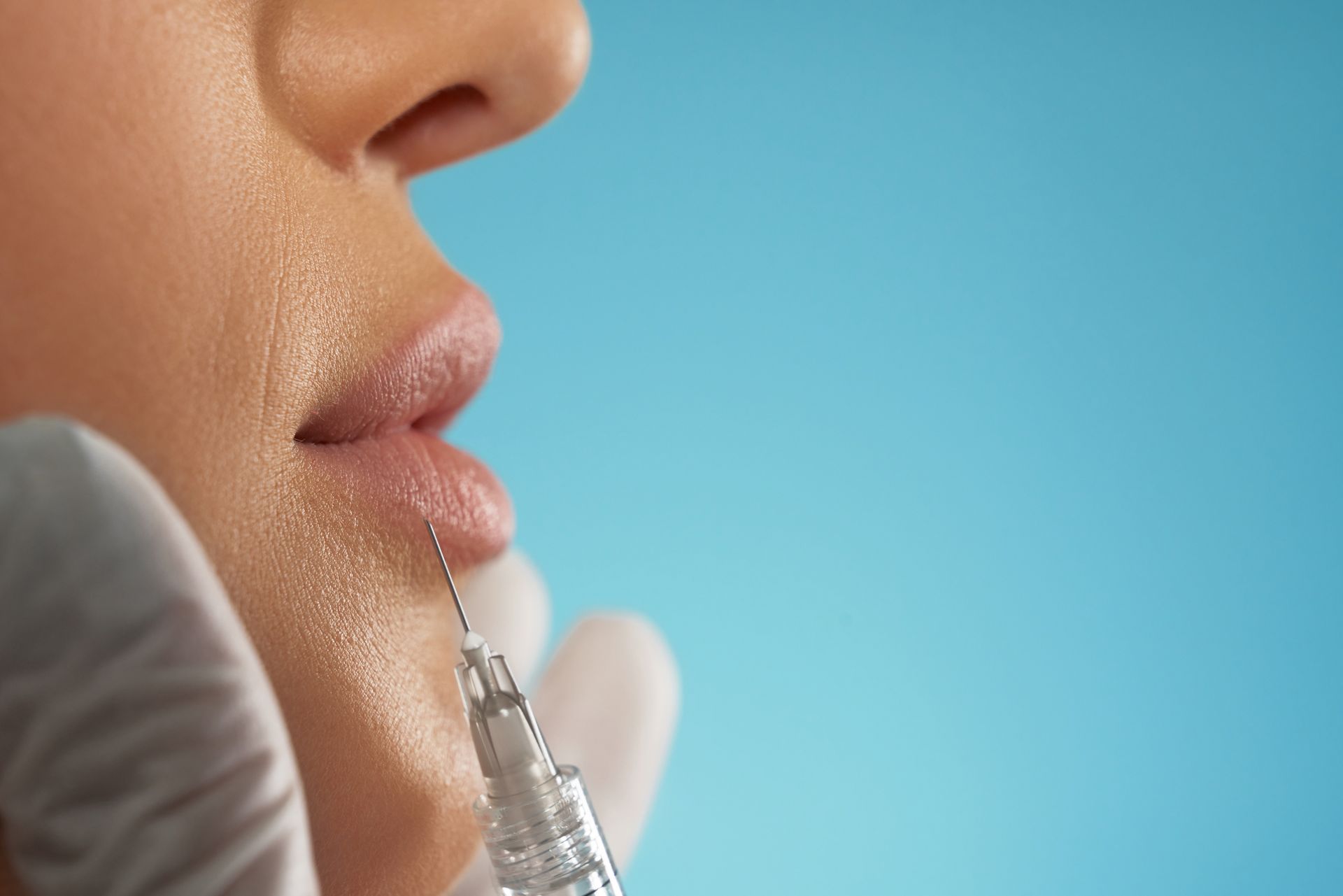 Needle injecting filler into a person's lip. Blue background. Close-up.