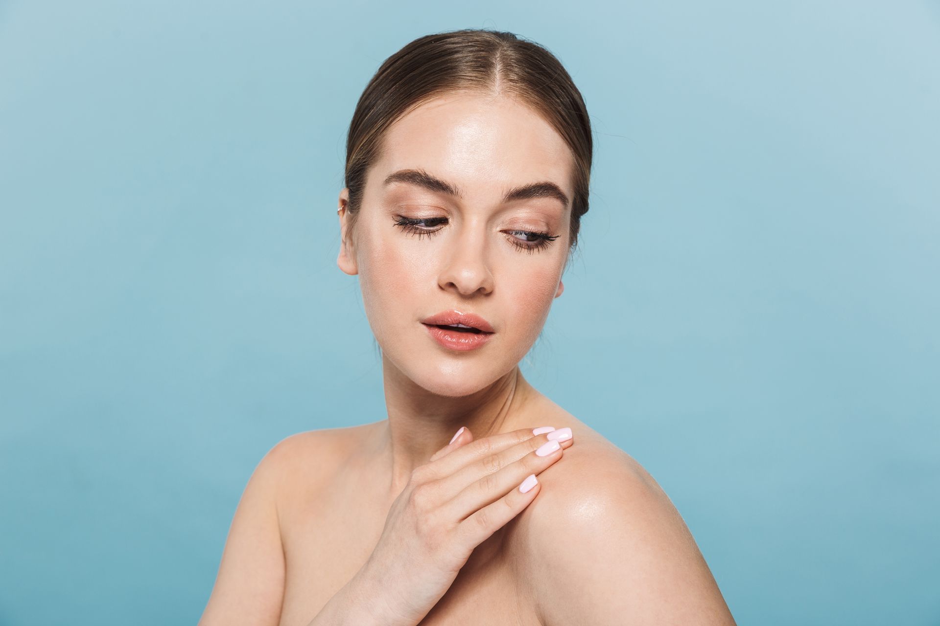 A woman with curly hair and freckles is touching her face with her hand.