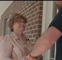 A woman wearing glasses is shaking hands with a man in front of a brick building