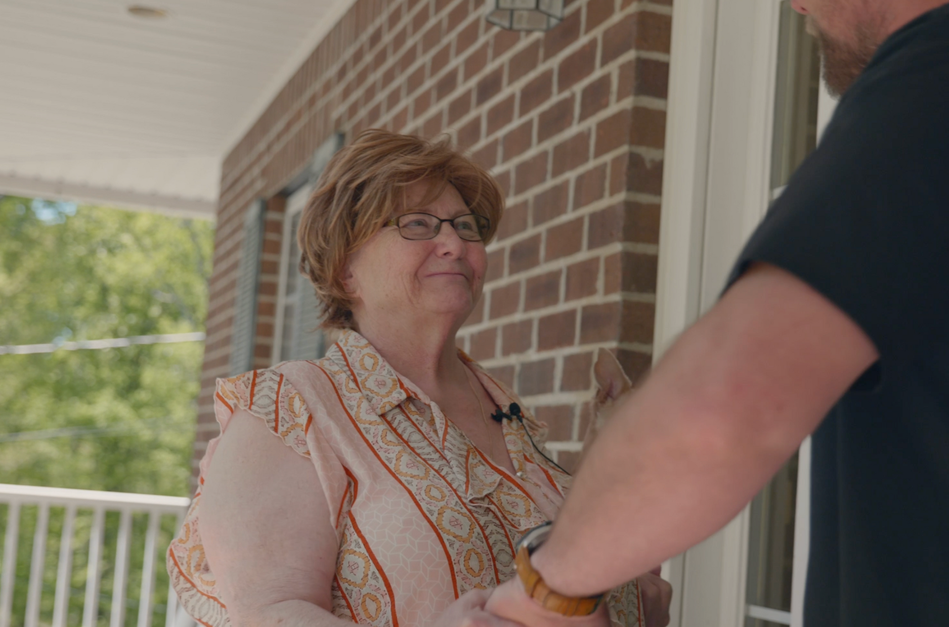 A man is shaking hands with an older woman on a porch.