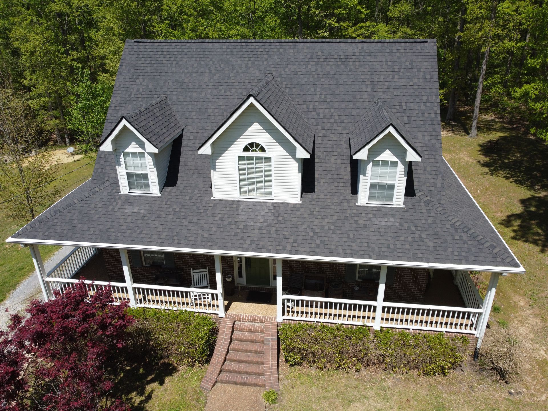 An aerial view of a large white house with a black roof and a porch.