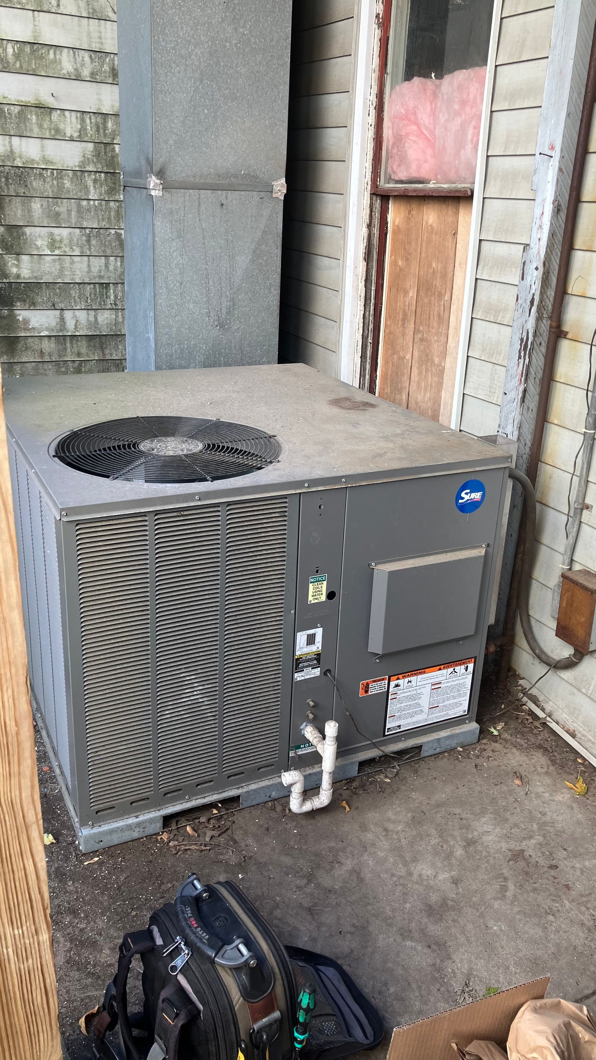 Air conditioning unit next to a duct in a narrow space, with tools in the foreground.