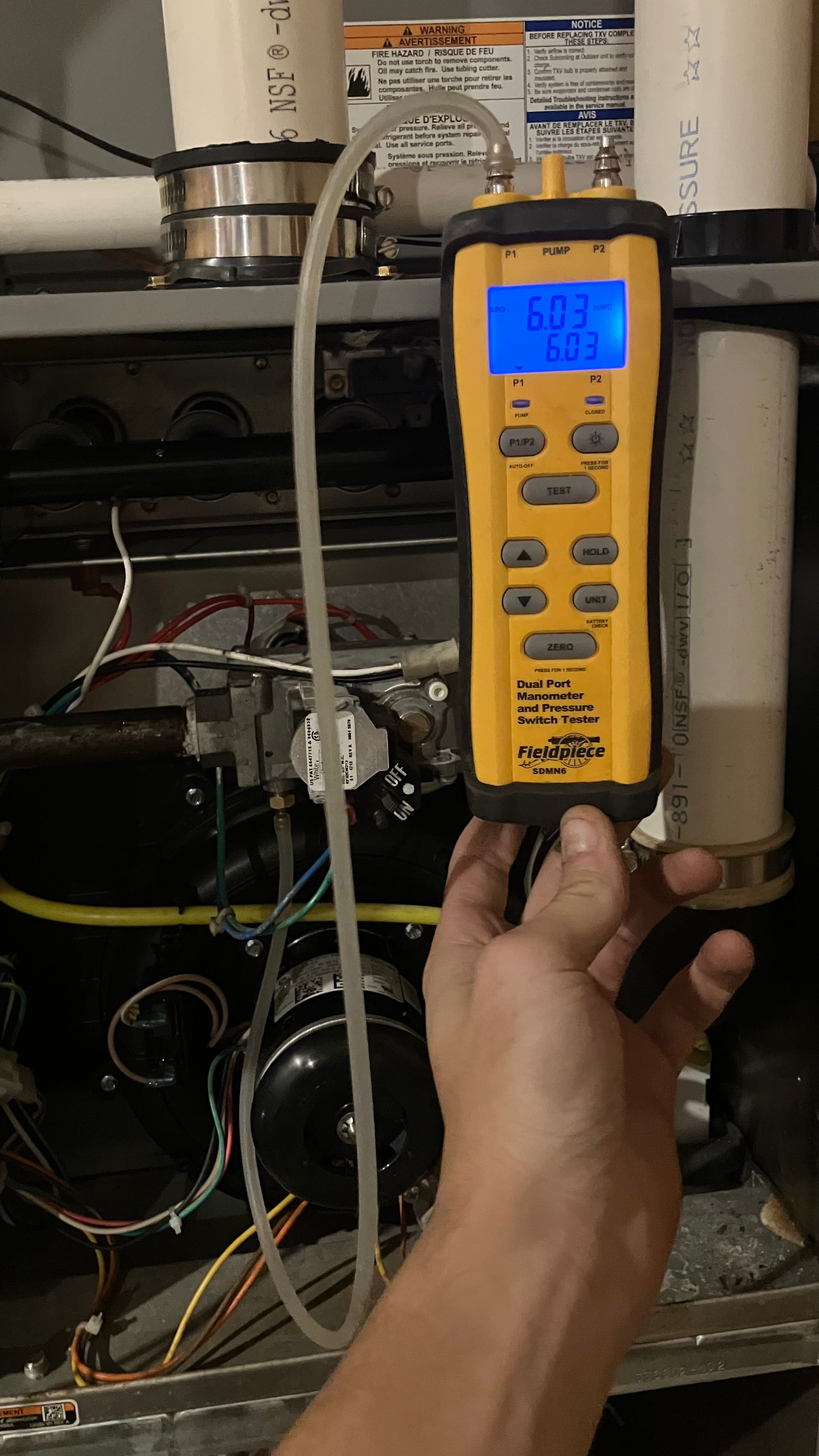 Hand holding a yellow digital manometer measuring the pressure of a furnace.