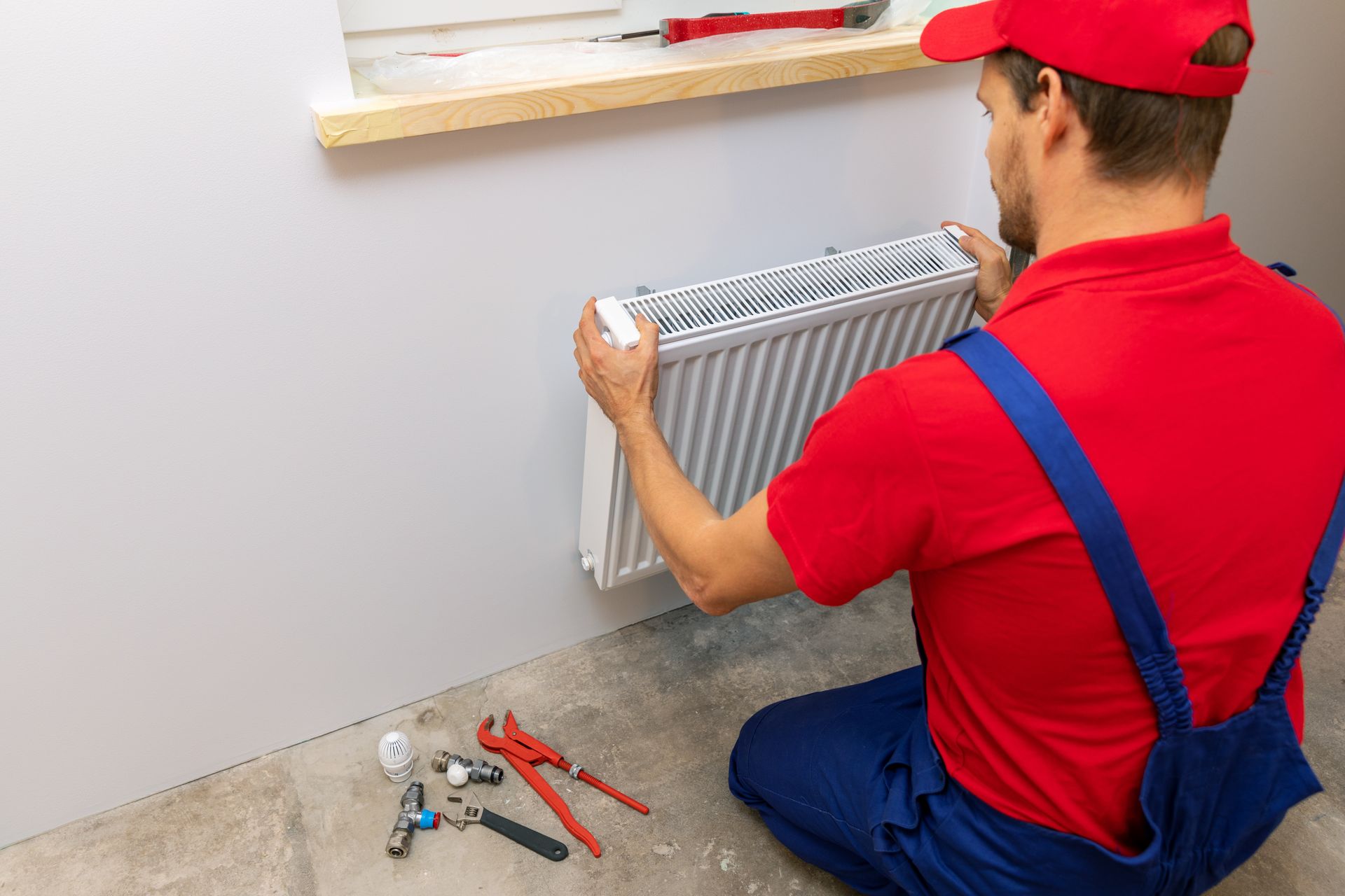 Plumber installing wall-mounted heating radiator with plumbing tools on floor.
