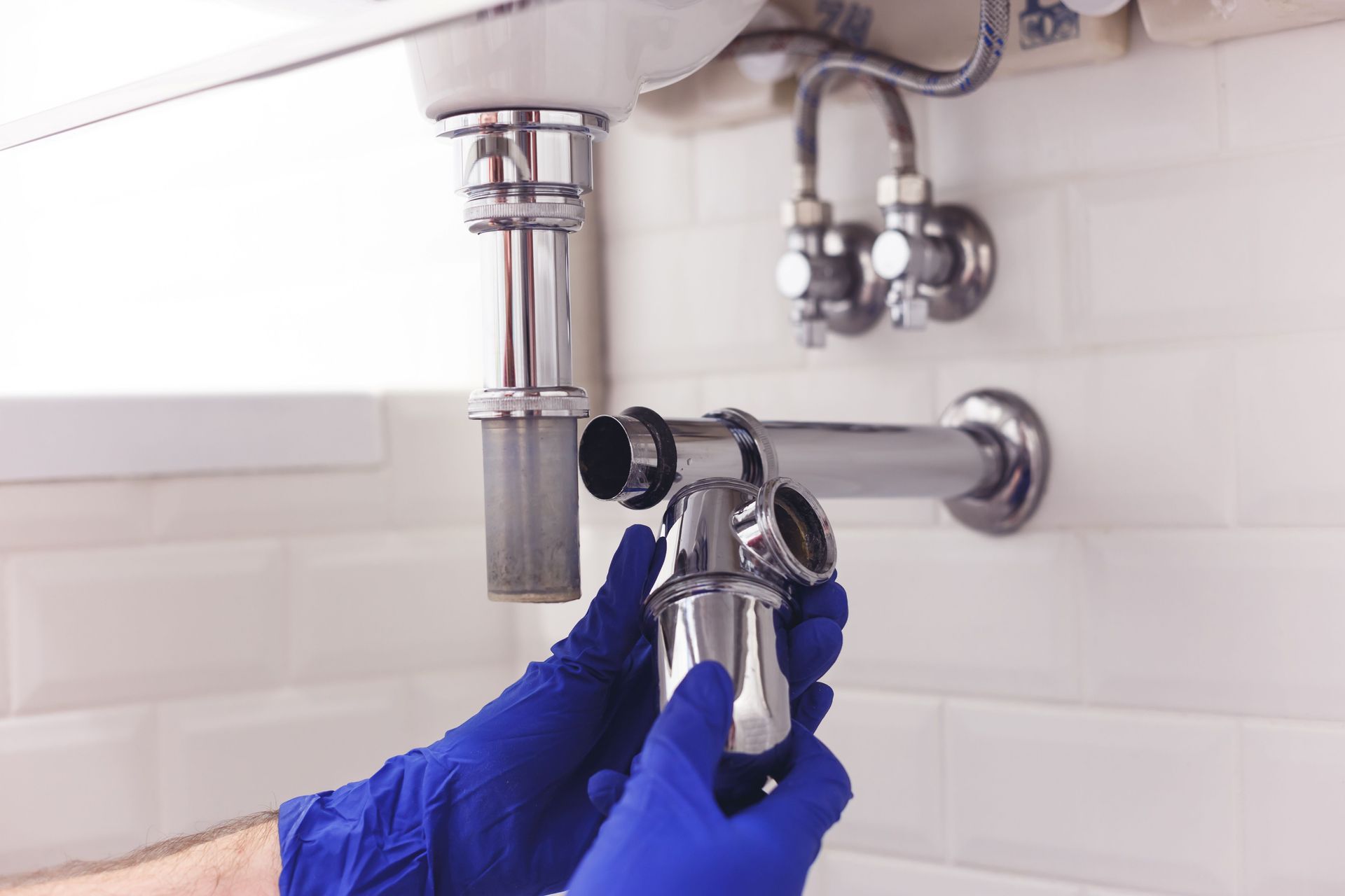 Blue-gloved hands tightening a chrome pipe fitting under a bathroom sink