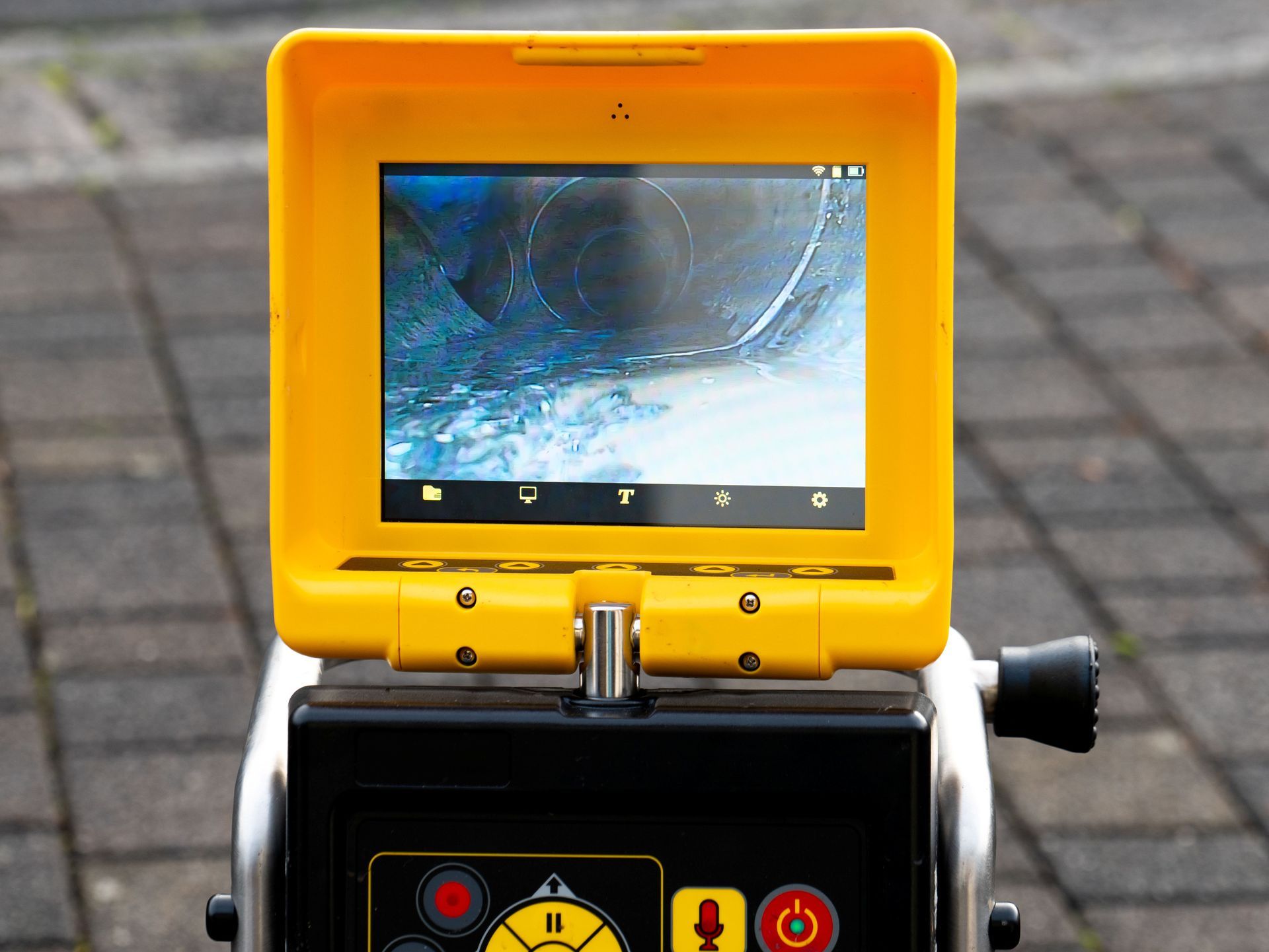 Yellow inspection camera with a small screen mounted on a black device outdoors on pavement