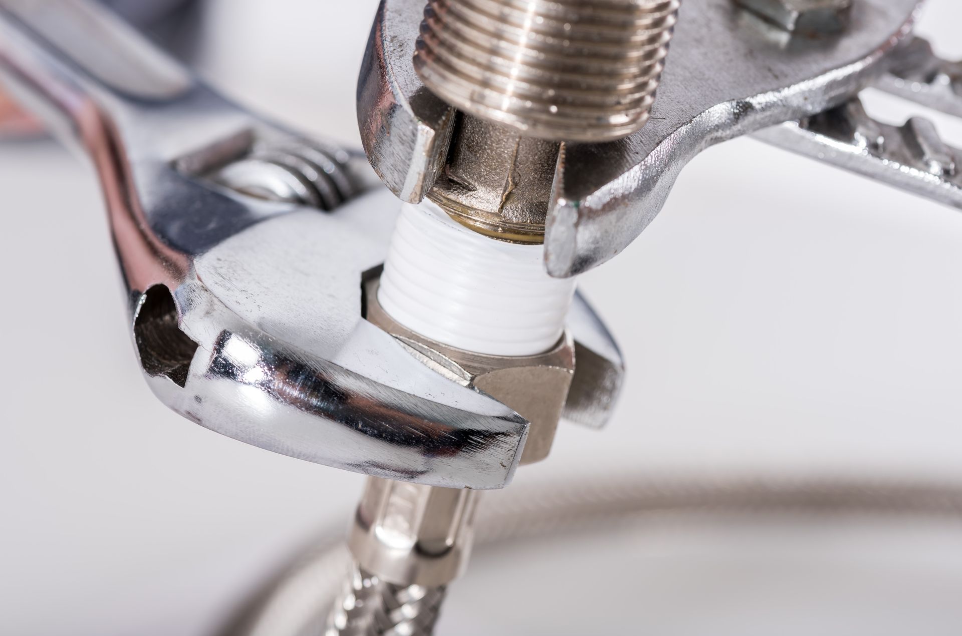 Close-up of a chrome wrench tightening a white plastic pipe fitting on a metal valve.
