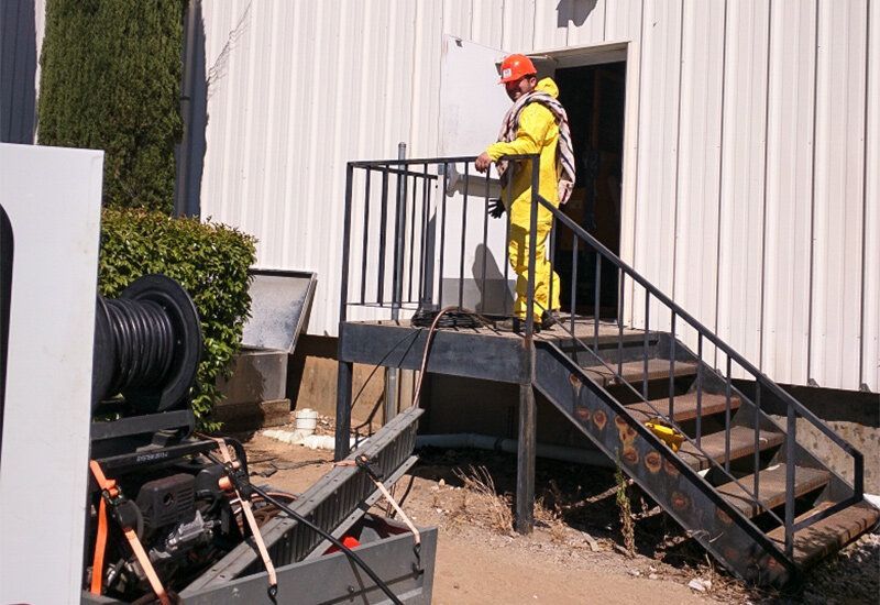 Worker in yellow safety gear stands on outdoor metal stairs beside a building.