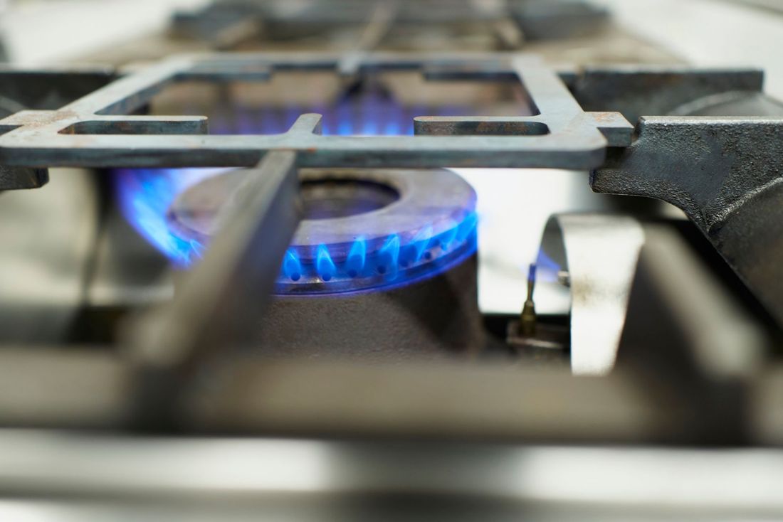 Bruciatore per fornello a gas con fiamme blu brillante, griglia in metallo e superficie in acciaio inossidabile.