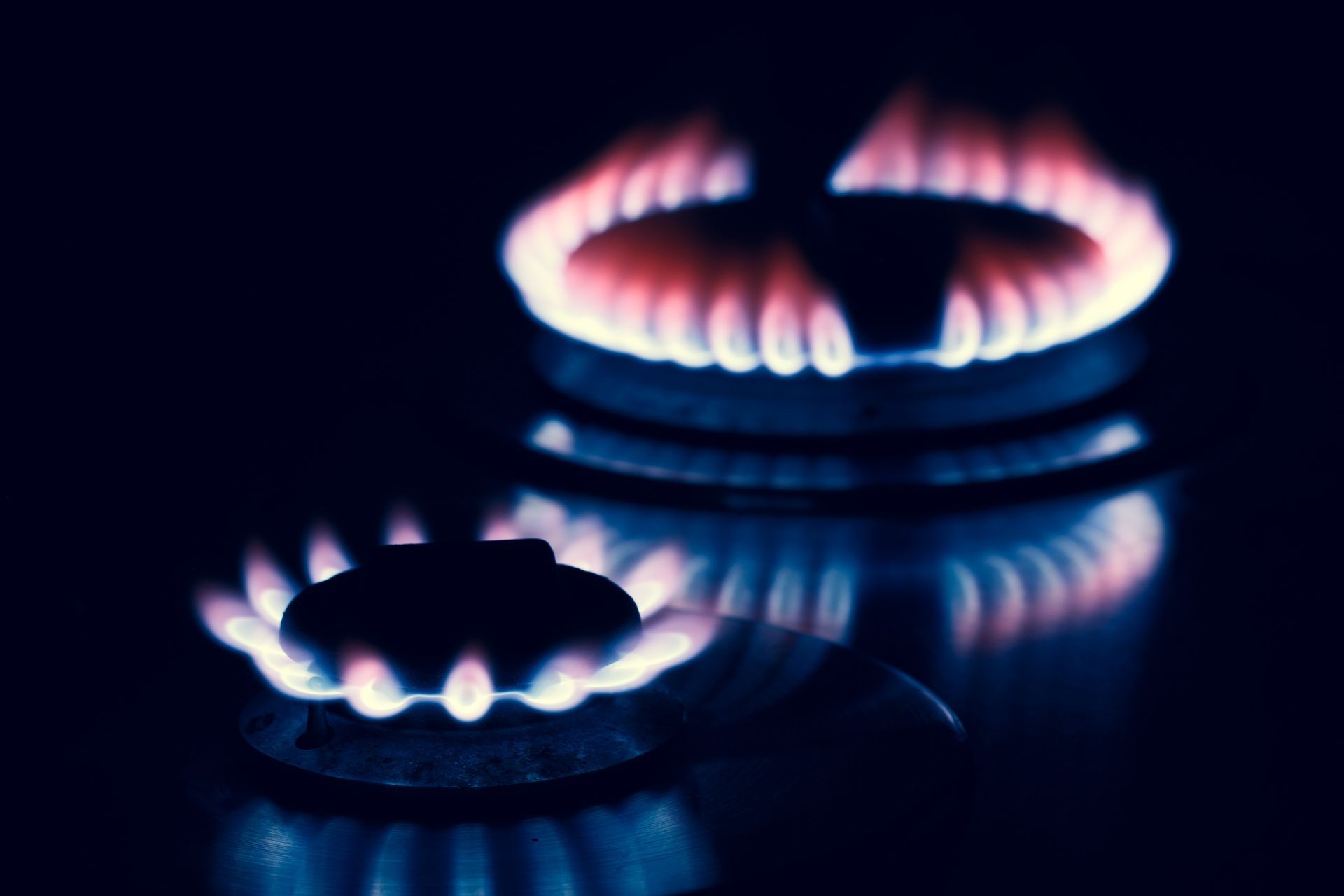 I fornelli a gas sono accesi e emettono fiamme blu e rosse su uno sfondo scuro.