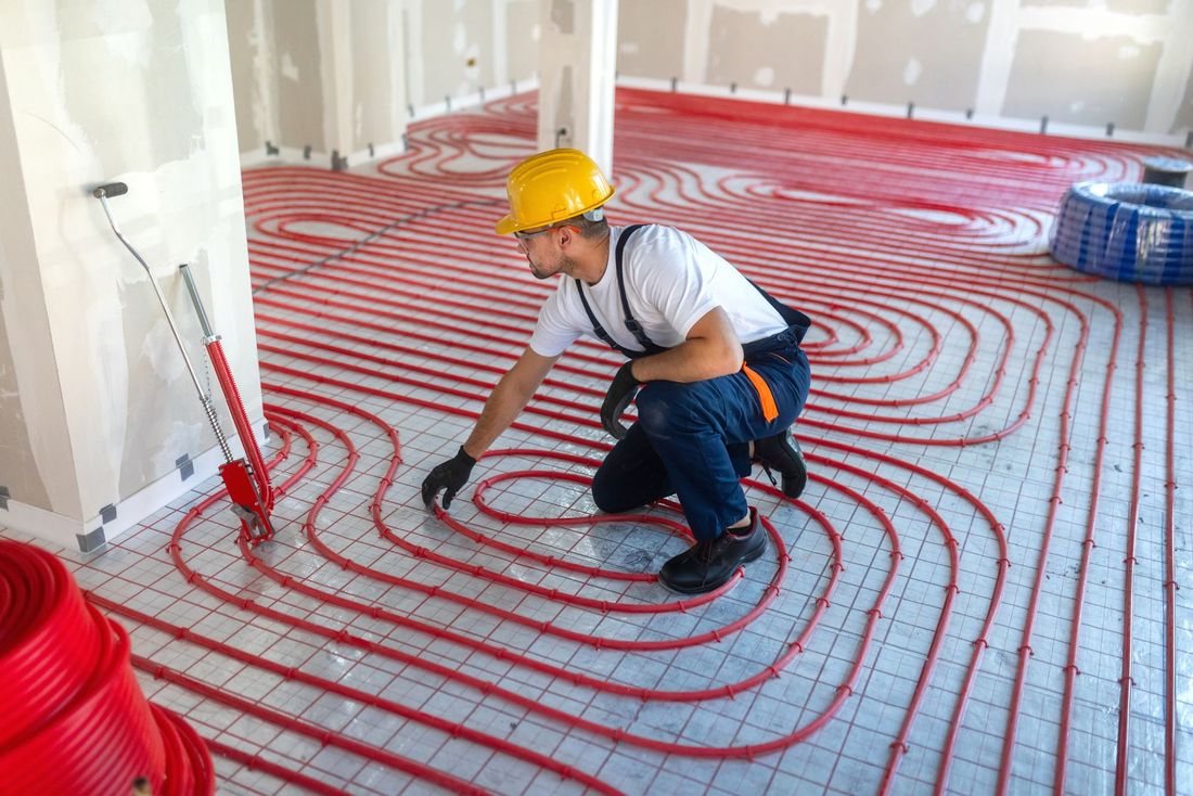 Un operaio edile installa tubi rossi per il riscaldamento a pavimento in una stanza in costruzione.