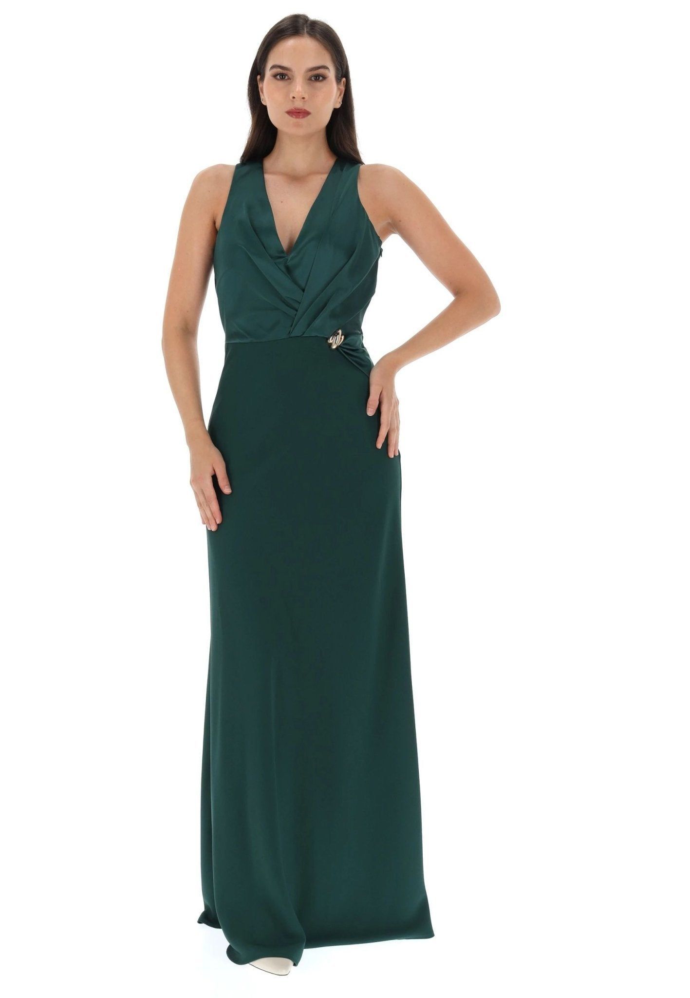 Donna che indossa un abito da sera verde scuro, con una mano sul fianco, in piedi su uno sfondo bianco.