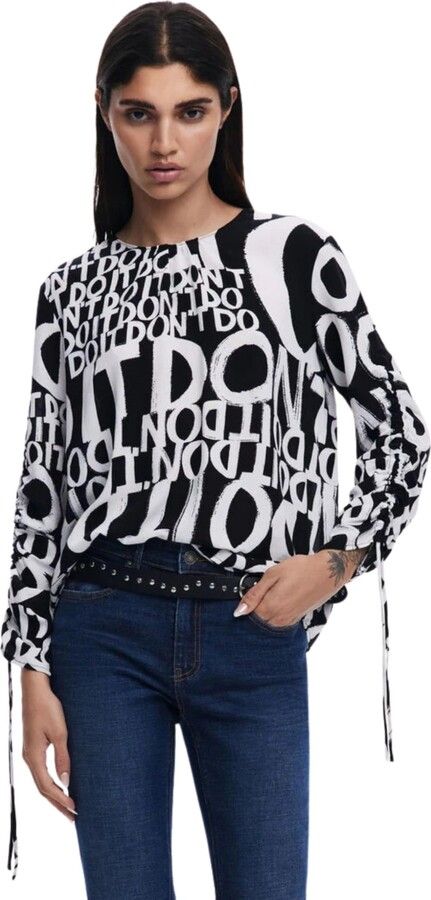 Donna in piedi, con indosso un top a fantasia bianca e nera e jeans scuri.