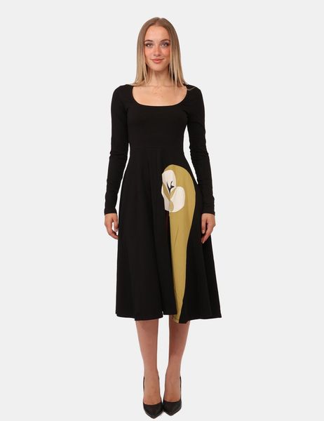 Donna con abito nero a maniche lunghe, decorazione laterale beige e tacchi neri.