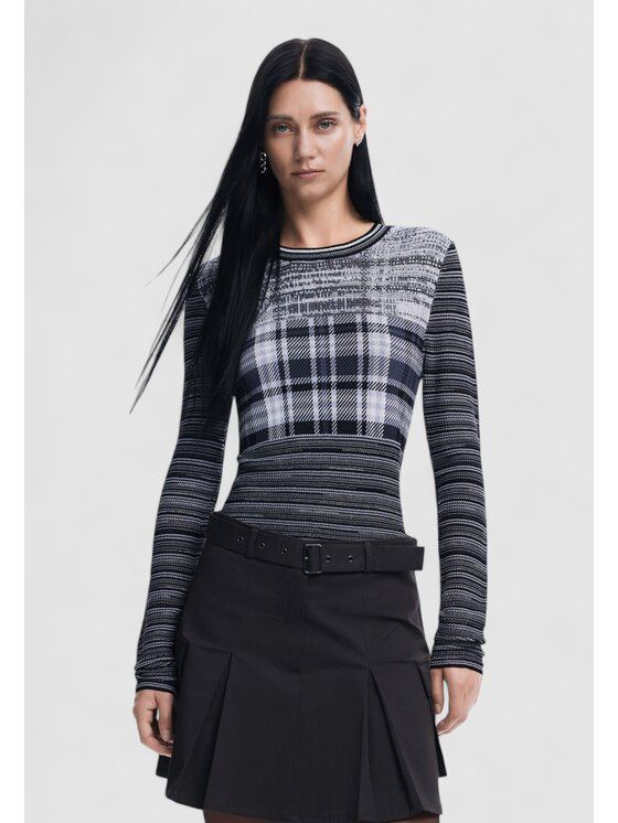 Donna che indossa un maglione scozzese e una gonna nera a pieghe, in posa in studio.