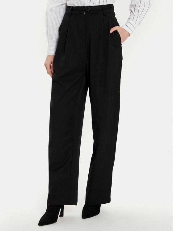 Donna in pantaloni neri a gamba larga, camicia bianca e stivali neri, in posa per una foto.