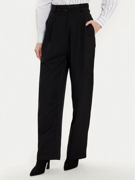 Donna in pantaloni neri a gamba larga, camicia bianca e stivali neri, in posa per una foto.
