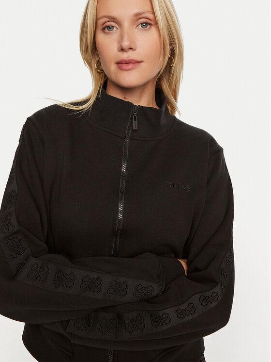 Donna con una felpa nera con cerniera e logo, che guarda la telecamera.