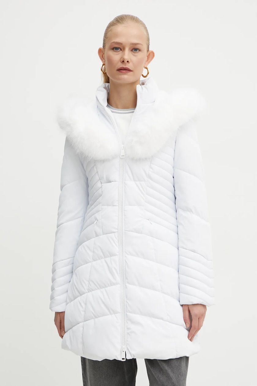 Donna in piumino bianco con collo di pelliccia, in piedi, che guarda avanti.