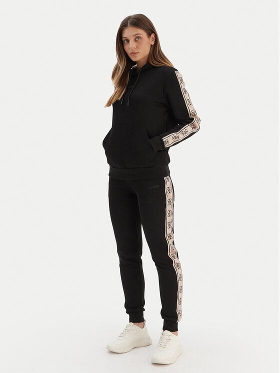 Donna in tuta nera con striscia del logo in posa su uno sfondo bianco.