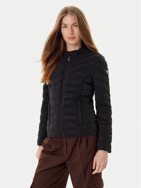 Donna con giacca trapuntata nera e pantaloni marroni, in piedi su uno sfondo bianco.