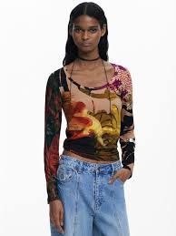 Donna con maglia a maniche lunghe stampata e jeans chiari, in posa su uno sfondo bianco.