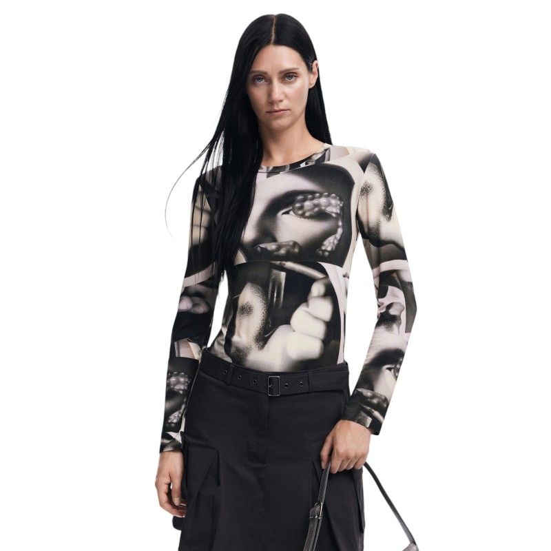 Donna che indossa una maglietta a maniche lunghe con una stampa di un volto in bianco e nero, gonna nera e una borsa in mano.