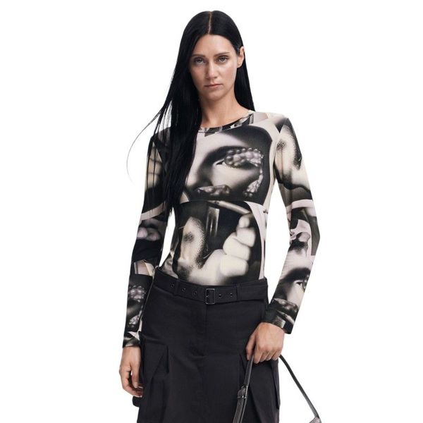 Donna che indossa una maglietta a maniche lunghe con una stampa di un volto in bianco e nero, gonna nera e una borsa in mano.