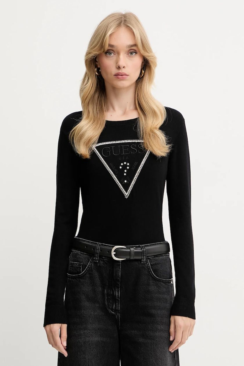 Donna che indossa un maglione nero con logo in cristallo, jeans neri e cintura.