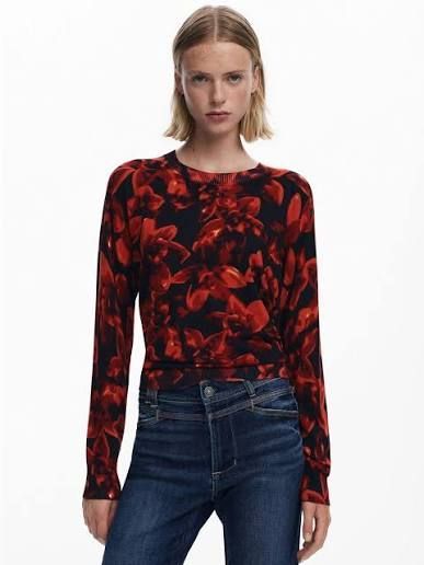 Donna con top floreale rosso e nero, jeans blu scuro.