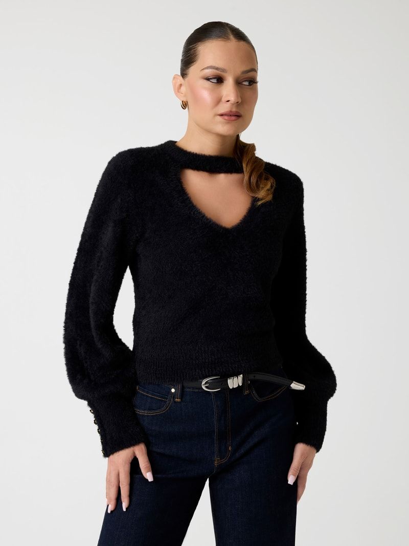 Donna con maglione nero soffice con scollatura traforata e jeans scuri.